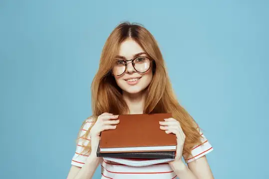 Энергичная студентка с блокнотами и в очках позирует на синем фоне