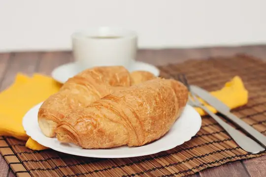 Свежие круассаны на белой тарелке рядом с чашкой кофе