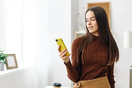 Девушка сидит за столом и улыбается, глядя в свой мобильный телефон