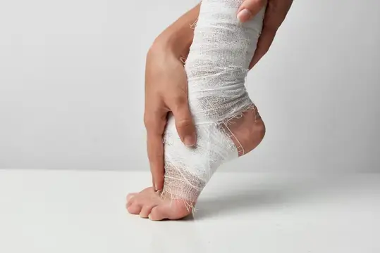 Руки бинтуют голеностоп эластичным бинтом на белом фоне