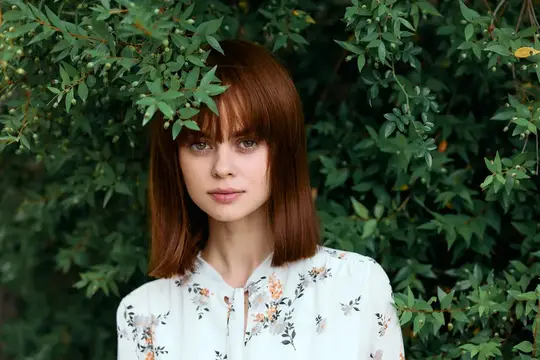 Яркая рыжеволосая женщина позирует на фоне цветущего кустарника с красочными цветами
