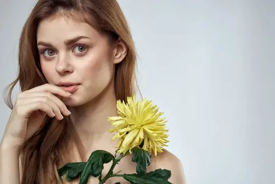 Молодая женщина с жёлтой хризантемой у лица на сером фоне