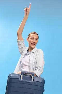 Улыбающаяся женщина с чемоданом поднимает руку вверх