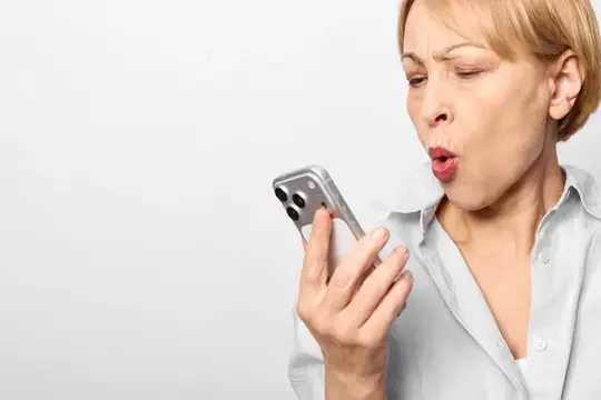 Женщина удивлена сообщением на смартфоне: держит устройство в руках, рот открыт, напряженное выражение лица от шока, принимает звонок или сообщение