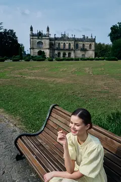 Улыбающаяся девушка сидит на скамейке в парке перед старинным замком
