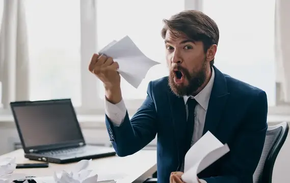 Разъяренный бородатый мужчина в костюме рвет бумаги в офисе