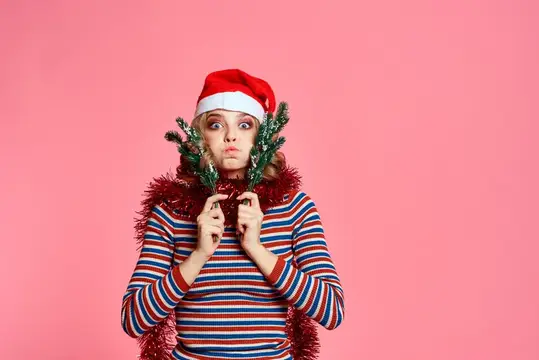 Девушка в новогодней шапке с ёлочными ветками на розовом фоне