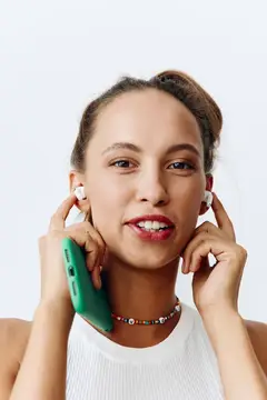 Улыбающаяся девушка в белых наушниках держит зеленый смартфон