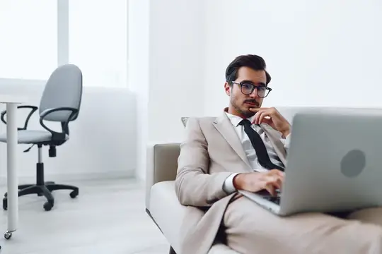 Задумчивый мужчина в очках работает за ноутбуком в светлом офисе