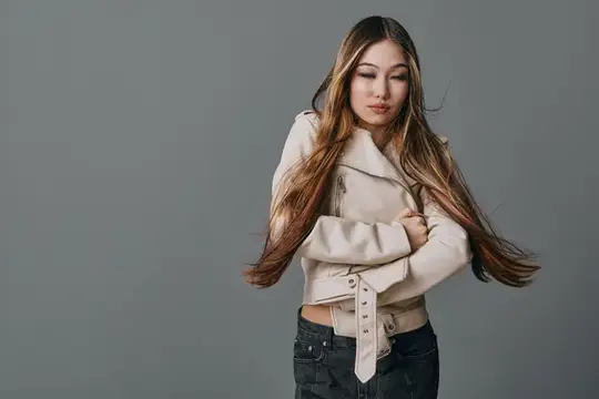 Азиатская девушка с длинными волосами в светлой куртке на сером фоне