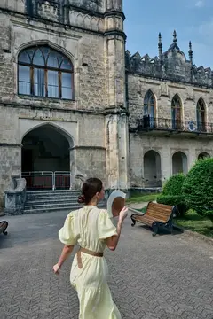 Девушка в светлом платье с шляпой на фоне старинного замка
