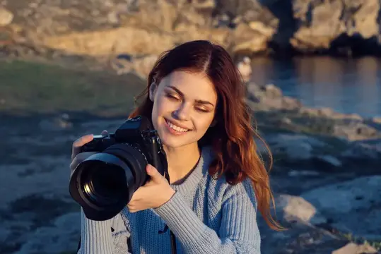 Улыбающаяся девушка с фотокамерой на скалистом берегу
