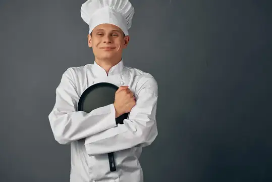 Весёлый шеф-повар в форме держит сковороду в руках в ресторане, занимаясь приготовлением пищи