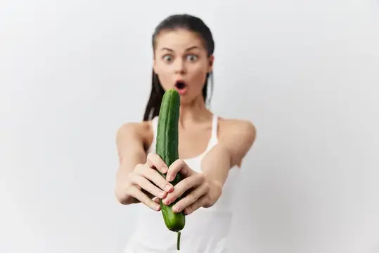 Удивлённая девушка с огурцом в руках на белом фоне