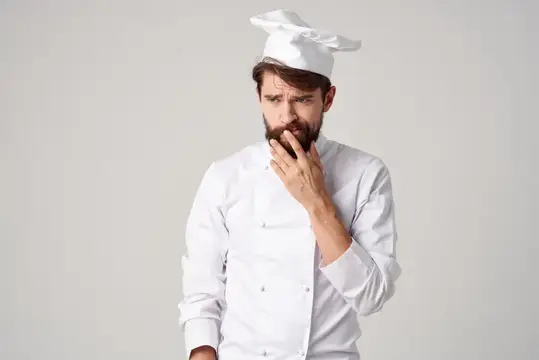 Задумчивый бородатый повар в белом колпаке на сером фоне