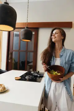 Улыбающаяся темноволосая женщина с салатом на светлой кухне