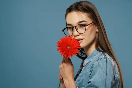 Привлекательная женщина в очках с красным цветком в качестве украшения на модном синем фоне