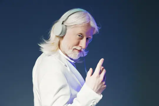 Седой мужчина в белом пиджаке слушает музыку в наушниках