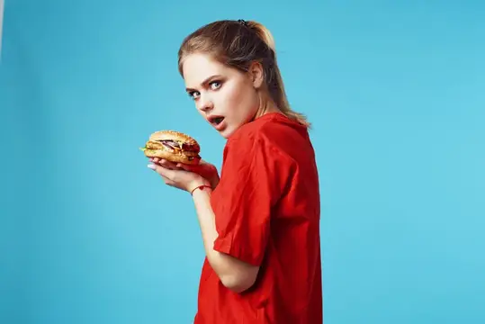 Удивлённая девушка в красной футболке с бургером на голубом фоне