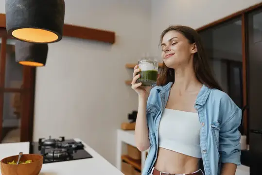 Молодая женщина с наслаждением пьёт зелёный смузи на светлой кухне