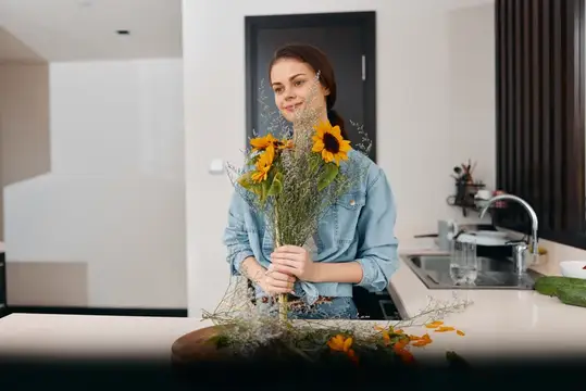 Молодая женщина с букетом подсолнухов стоит на светлой кухне