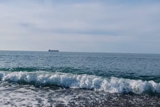 Волна с белой пеной на фоне моря и грузового судна