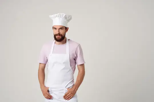 Бородатый мужчина в поварском колпаке и фартуке на светлом фоне