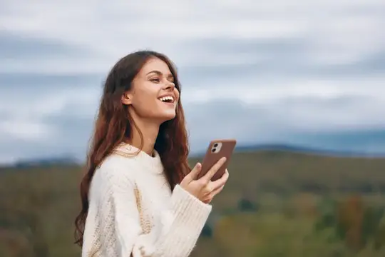 Смеющаяся девушка со смартфоном на фоне холмов