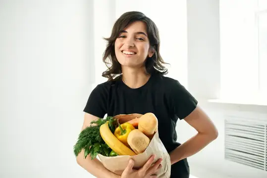 Улыбающаяся девушка с бумажным пакетом свежих овощей и хлеба
