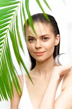 Молодая женщина с пальмовым листом и флаконом косметики