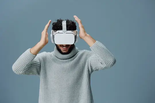 Улыбающийся темноволосый мужчина в VR-очках поднял руки