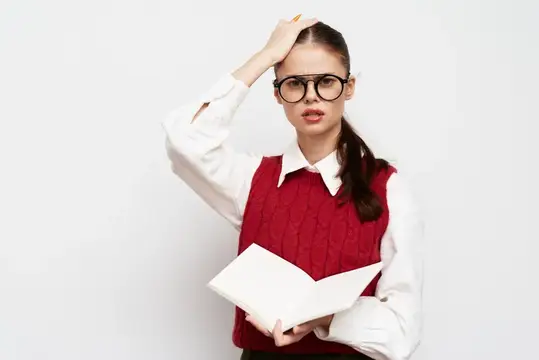 Уставшая девушка в очках с книгой держится за голову
