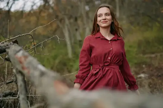 Улыбающаяся девушка в бордовом платье гуляет по осеннему лесу