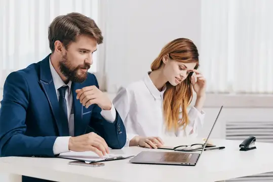 Бородатый мужчина в костюме и рыжеволосая женщина работают за столом в офисе
