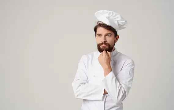 Задумчивый бородатый повар в белом колпаке на сером фоне