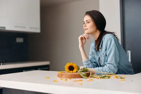 Задумчивая девушка с подсолнухом за столом на светлой кухне