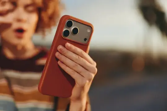 Рыжеволосая девушка с удивлением смотрит на смартфон в терракотовом чехле