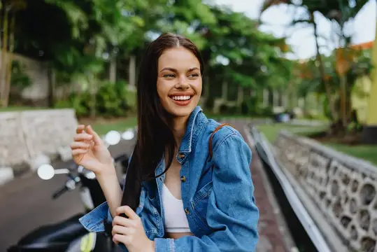 Улыбающаяся темноволосая девушка в джинсовой куртке на улице