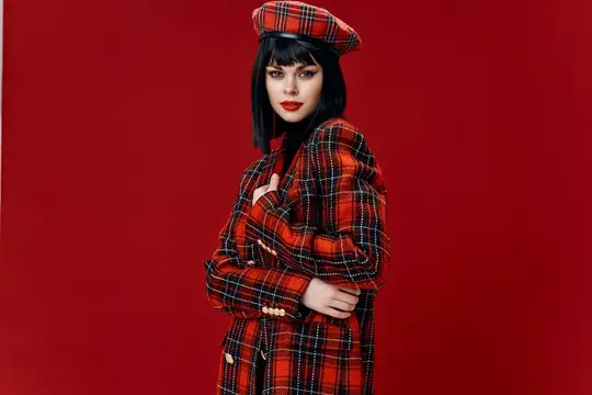 Молодая женщина в клетчатом берете и пальто на красном фоне