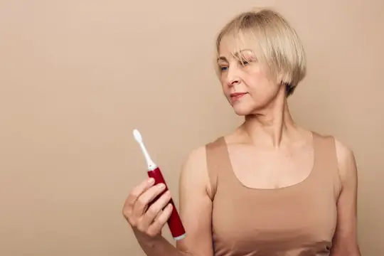 Светловолосая женщина держит красную электрическую зубную щетку