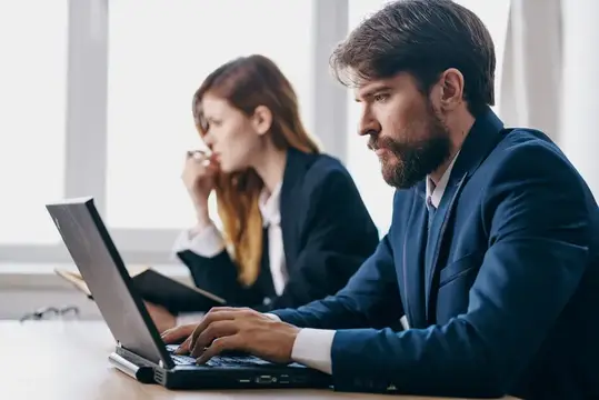 Бородатый мужчина в костюме работает за ноутбуком в офисе