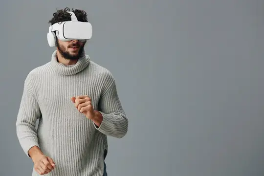 Бородатый мужчина в свитере и VR-очках на сером фоне