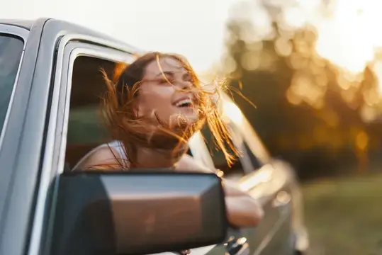 Счастливая женщина высунулась из окна машины на закате