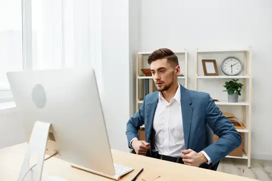 Мужчина в костюме работает за компьютером на рабочем столе, излучая уверенность в себе