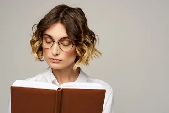 Молодая женщина в очках с книгой на сером фоне