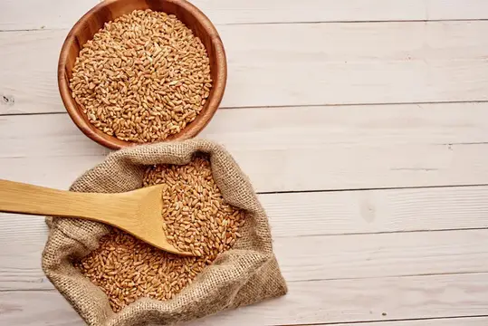 Деревянная миска и мешок с пшеничными зёрнами на светлом столе