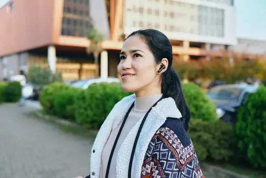Азиатская девушка в наушнике улыбается на городской улице