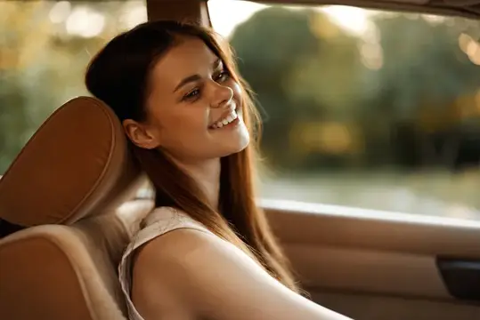 Улыбающаяся темноволосая девушка в автомобиле смотрит в окно
