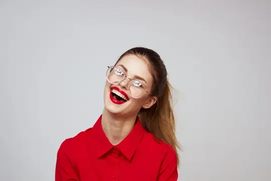 Модная женщина в красной рубашке на светлом фоне, весёлые эмоции, яркий макияж, очки, привлекательная внешность, сексуальный взгляд