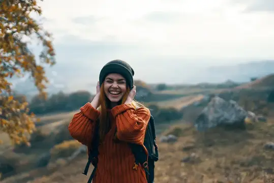 Улыбающаяся девушка в оранжевом свитере и шапке на осенней прогулке